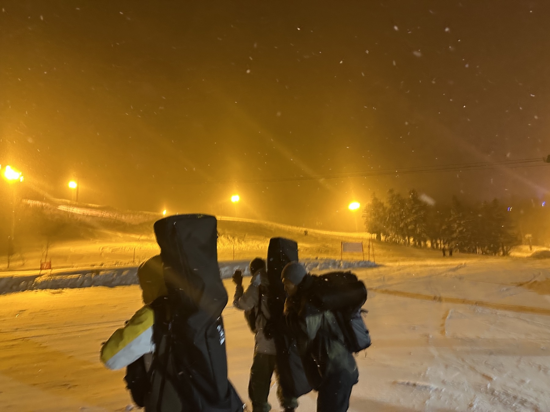 Walking with snowboards under orange lights at Teine
